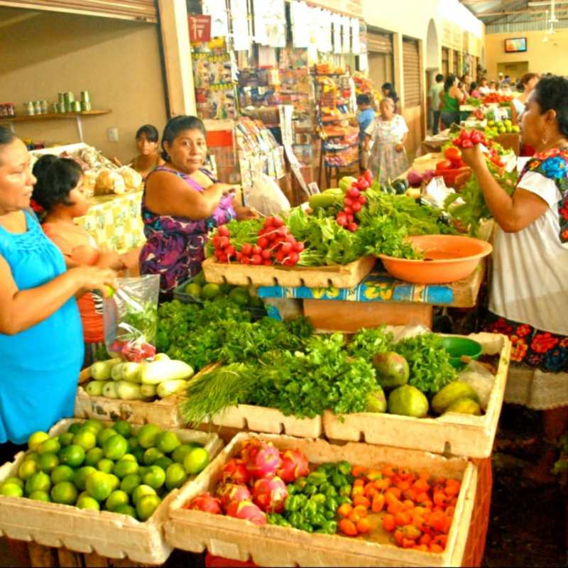 a woman standing in front of a store filled with lots of produce
