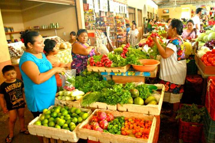 a woman standing in front of a store filled with lots of produce